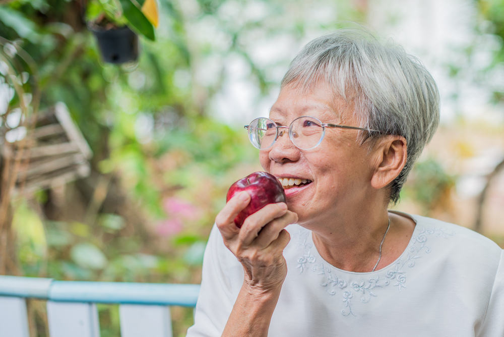 Elder lady with dental implants eating an apple