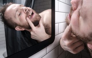 Man opened his mouth and carefully examines the absence of a tooth in mirror