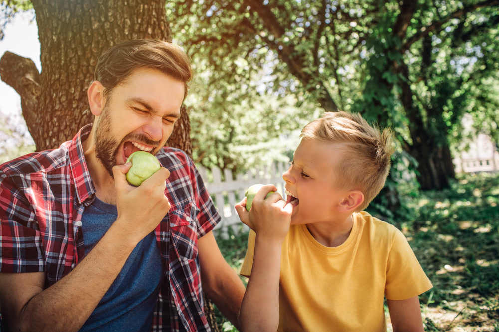 father and son sitting together and eating apples (Should I Replace My Missing Teeth)